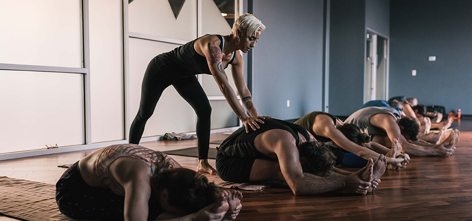 A yoga instructor adjusts a practitioner in an ashtanga class