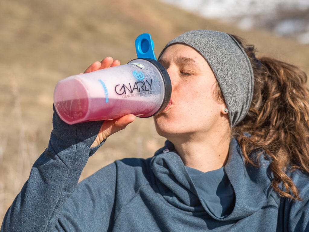 A woman drinks a sport recovery drink in the mountains